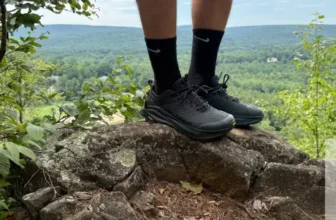 Standing on top of a rock wearing Altra Olympus 6 during testing, view of summit in background