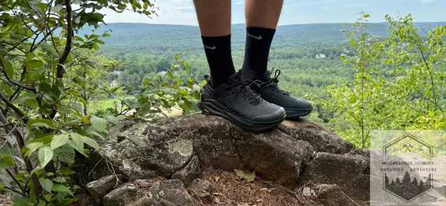 Standing on top of a rock wearing Altra Olympus 6 during testing, view of summit in background